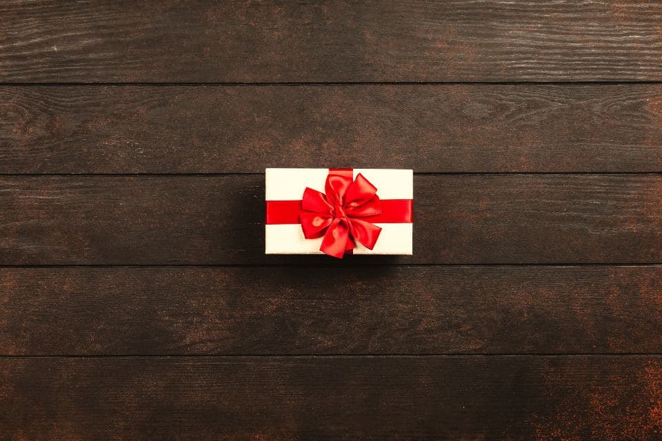 A wrapped gift box with a red ribbon on a dark wooden table